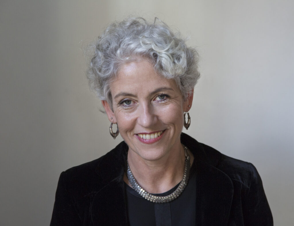 Woman with black jacket and short, grey hair smiling to camera
