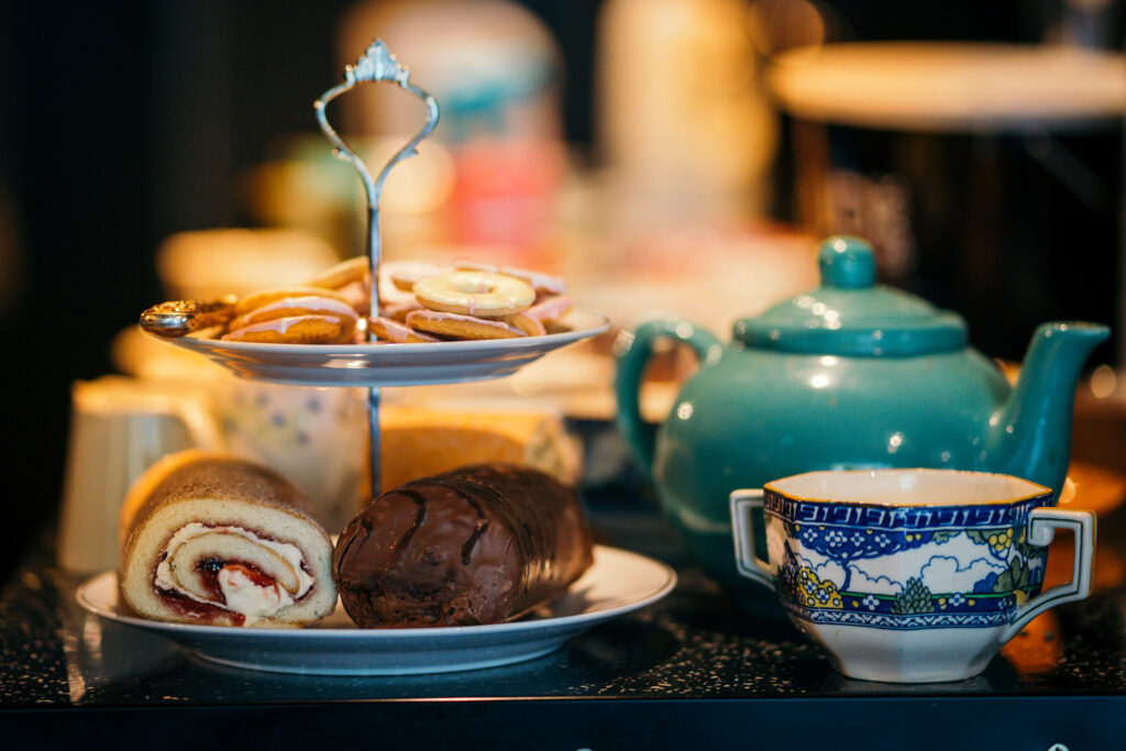 A pot and cup of tea with a small carousel of cakes, blurred background